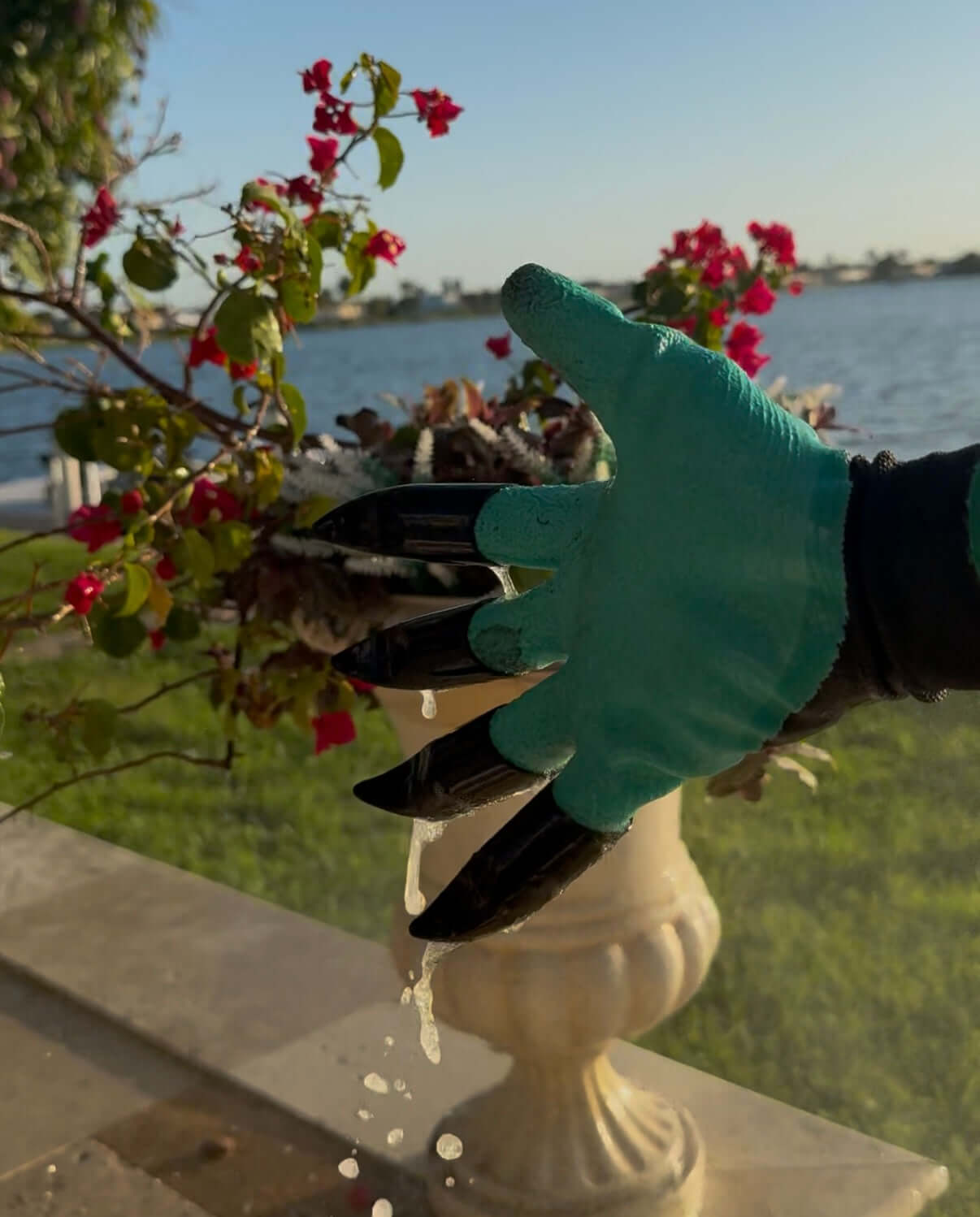 Gardening gloves with claws in turquoise, showcasing hand protection while watering plants near a scenic water view.